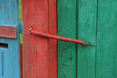 red metal spring closer on green wooden fence boards and doors on the street