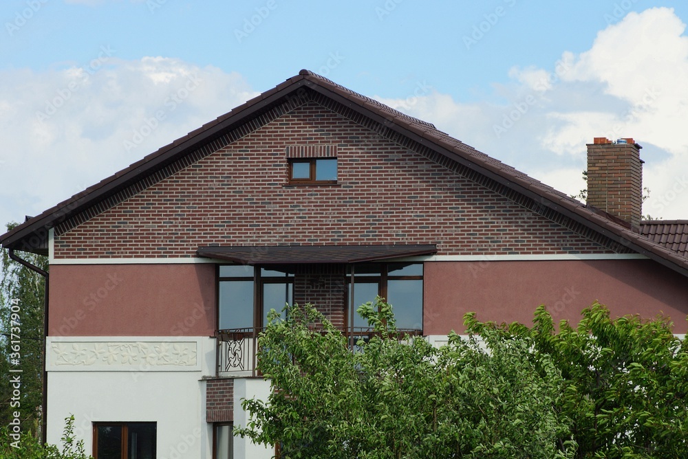 brown brick loft of a private house with windows in green vegetation against a blue sky