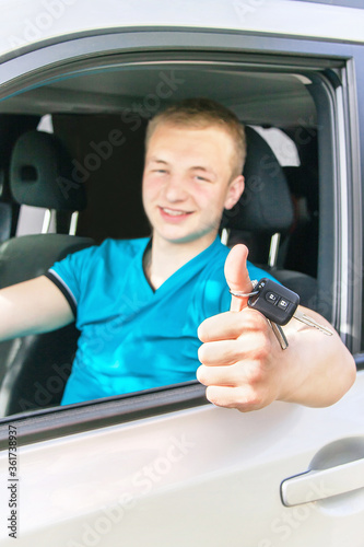 Car driver. Caucasian teen boy showing thumbs up, car key and new car.