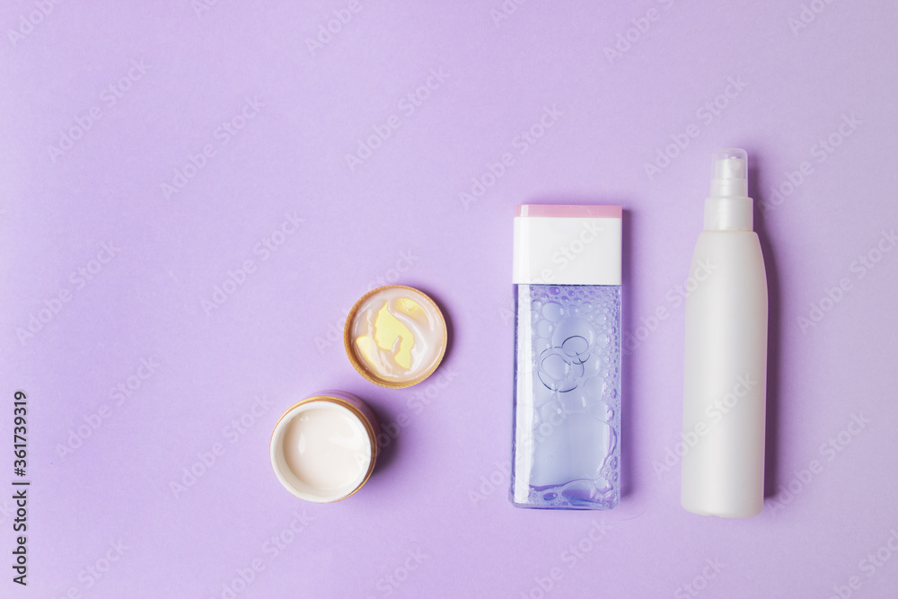 two cosmetic bottles and opened jar with cream on purple colored paper background with copy space two cosmetic bottles and opened jar with cream on purple colored paper background with copy space
