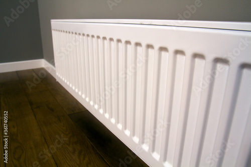 White metal heating radiator mounted on gray wall inside a room.