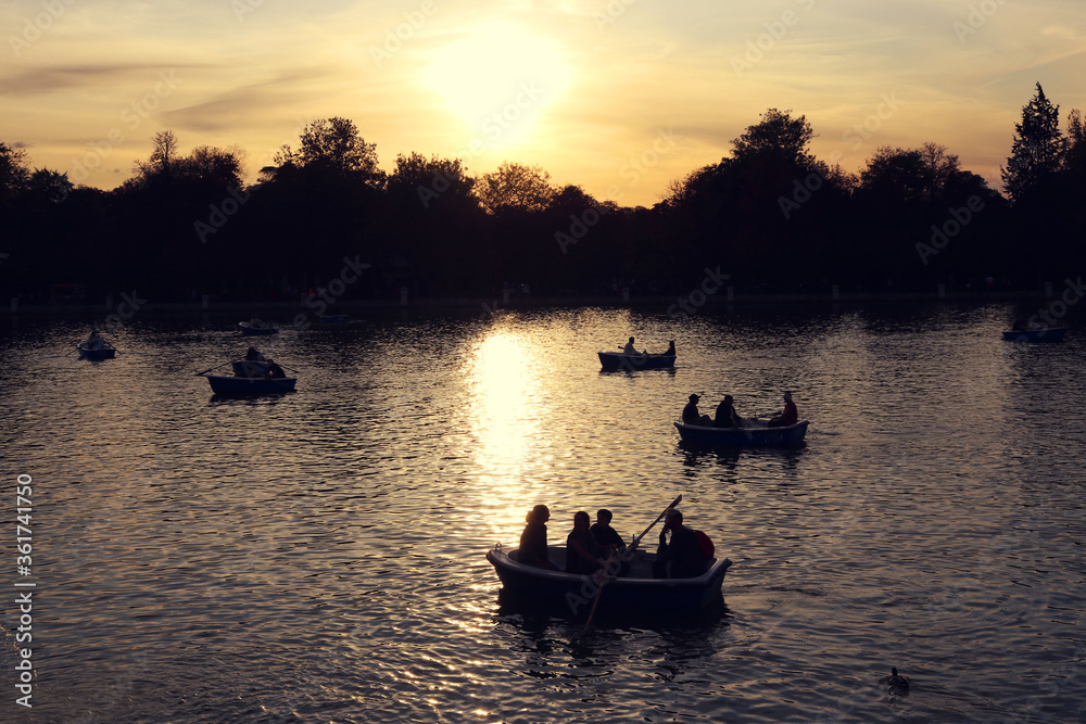 sunset in the lake of the park with people paddling on the boats and trees in the background - golden hour at Retiro park