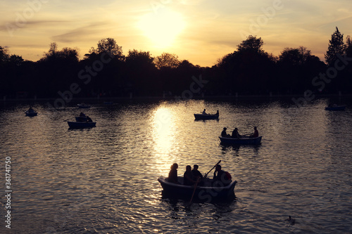 sunset in the lake of the park with people paddling on the boats and trees in the background - golden hour at Retiro park