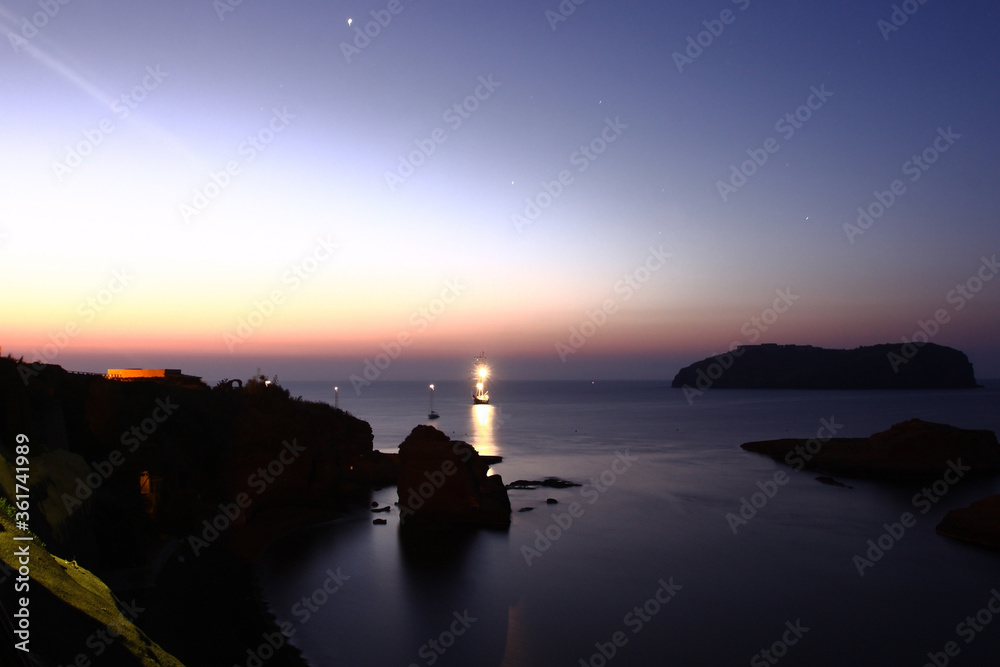 Fototapeta premium Ventotene, Italy - July 30, 2009: The sun rising at dawn on the island with boats in front of the island of Santo Stefano