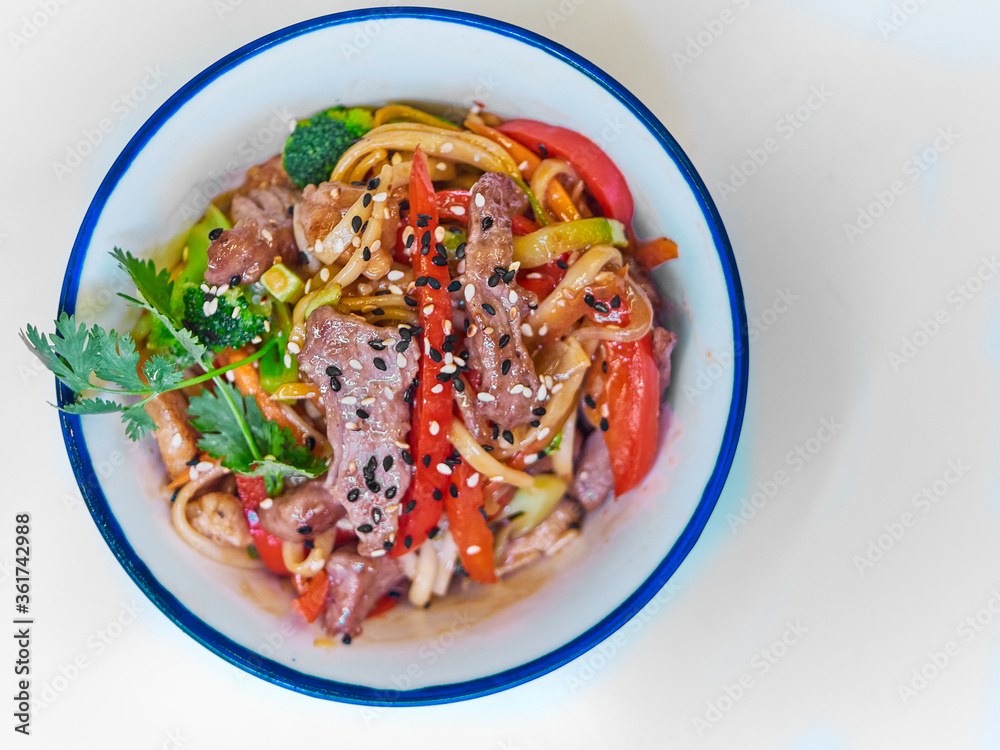 Udon noodles with meat in a plate on a white surface. With vegetables greens Udon noodles with meat in a plate on a white surface. With vegetables greens