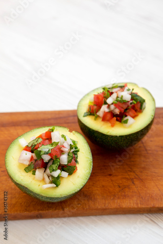 Homemade Pico de Gallo Stuffed Avocado on a rustic wooden board on a white wooden surface, side view. Copy space.