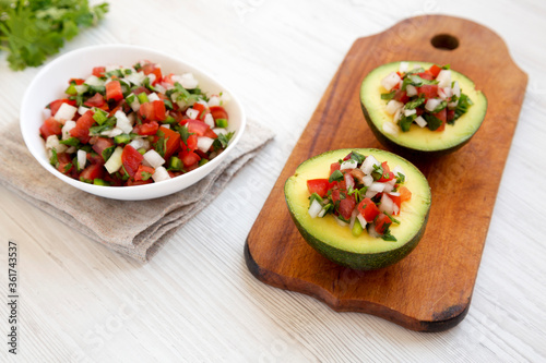 Homemade Pico de Gallo Stuffed Avocado on a rustic wooden board on a white wooden table, low angle view.
