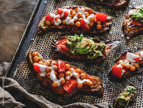 Baked sweet potato toasts with roasted chickpeas, tomatoes, goat cheese, sauce guacamole, avocado, seedlings on baking tray over brown background. Healthy vegan food, clean eating, top view