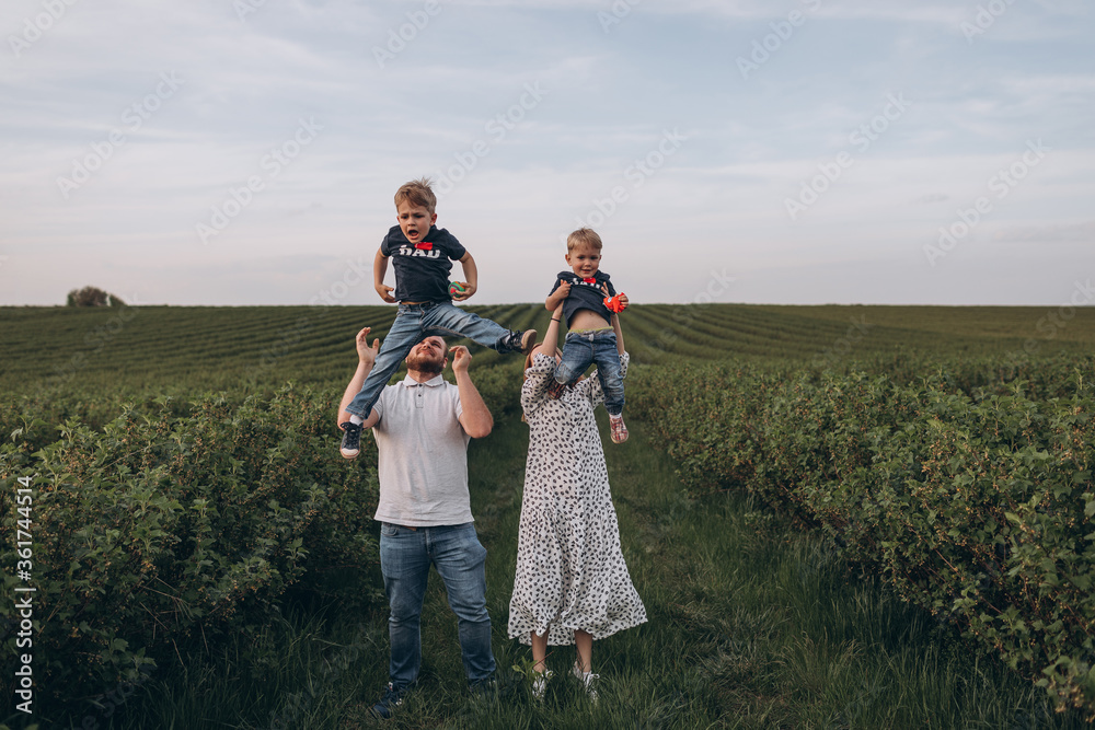 Big young happy family in the field on the nature. Mom, dad and 2 sons are having fun, running, fooling around together. Happiness and smiles around