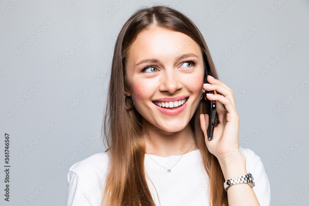 Smiling woman talking on the phone isolated on a grey background Smiling woman talking on the phone isolated on a grey background