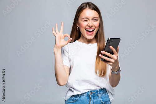 Happy gesturing young business woman with phone or support operator, showing okay gesture, isolated over white background