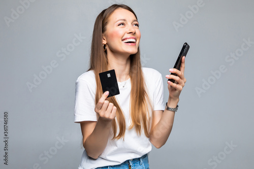Portrait of a smiling woman holding credit card and mobile phone while looking at camera isolated over white background