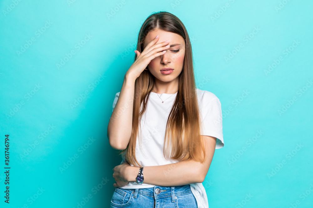 Exhausted woman touching head while standing with closed eyes on pastel blue background Exhausted woman touching head while standing with closed eyes on pastel blue background