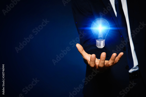 Idea concept. Businessman with glowing light bulb on dark background, closeup