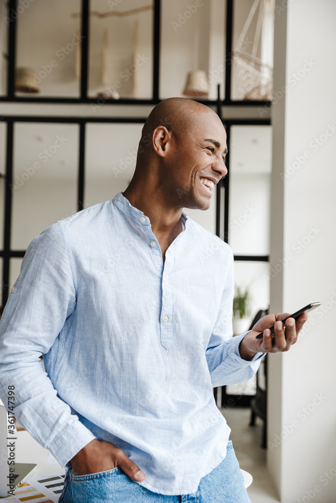 Photo of laughing african american man using mobile phone while working