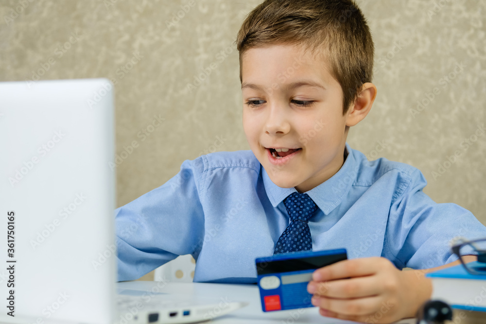 Children sitting in the office and working on a laptop. A little boy buys on the Internet. Young buyer pays by credit card. Children sitting in the office and working on a laptop. A little boy buys on the Internet. Young buyer pays by credit card.