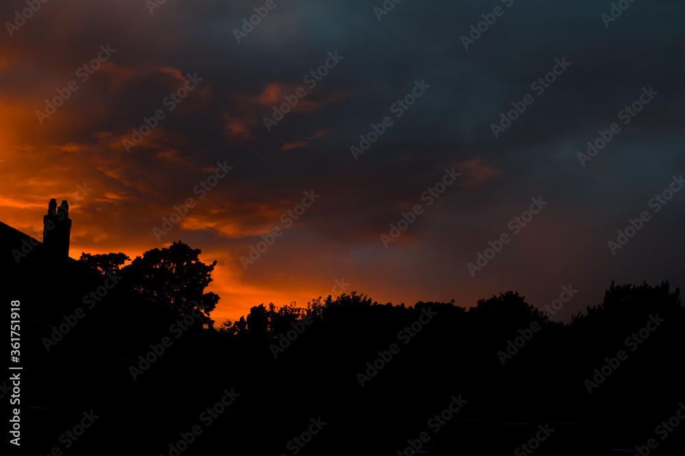 Silhouette of street of houses exterior in sunset with dark sky behind buildings Silhouette of street of houses exterior in sunset with dark sky behind buildings