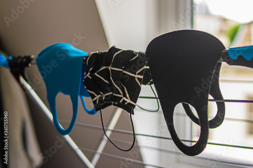 Photo of some reusable face masks colour blue and black hanging on a cloth rack while drying after washing. White background inside a house. Coronavirus outbreak