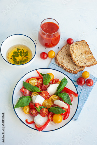 A light summer dinner. Red and yellow vegetable salad, tomato juice, basil sauce and toast. Vertical photo.