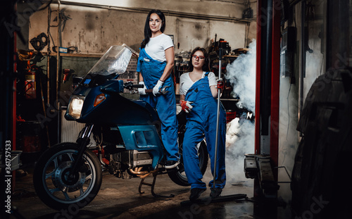 Two young female mechanic posing next to a sportbike in authentic workshop garage