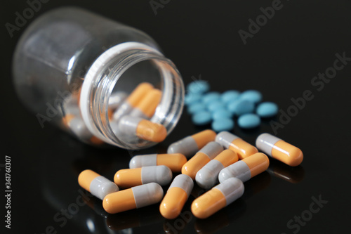Pills on a dark glass table, variation of medication in capsules and tablets scattered from a bottle. Concept of pharmacy, antibiotics, vitamins
