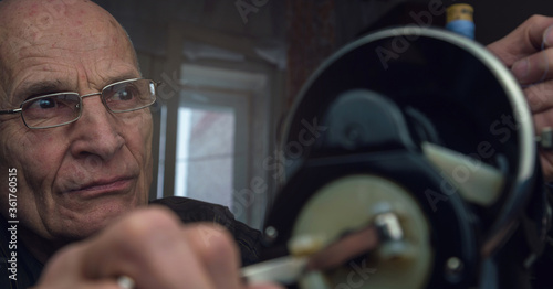 skilled senior man with glasses with vintage sewing machine in apartment