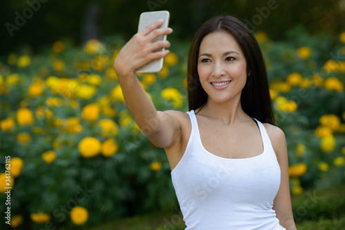 Happy beautiful Asian woman taking selfie at the park outdoors