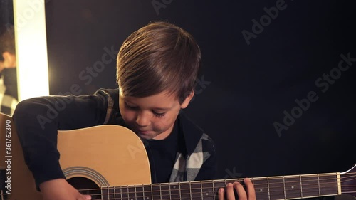 Beautiful smiling brunette boy is playing the acoustic guitar. Dark background.