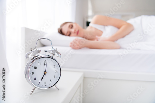 Profile blurry focus photo of charming lady lying sleeping bed white sheets blanket calm sure metal alarm clock will ring at seven o'clock morning work house monday bedroom indoors