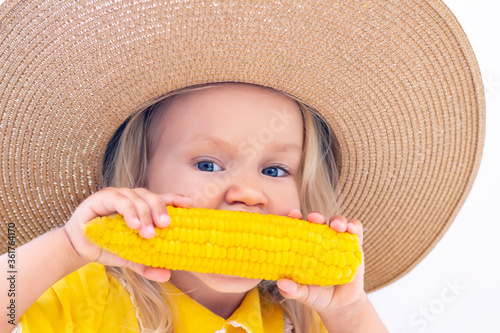 Child girl in a straw hat in yellow clothes eats corn  summer photo. on a light background
