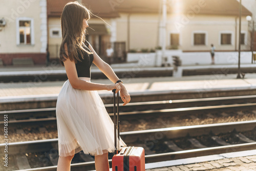 Female brunette traveler with red suitcase walking on raiway station photo