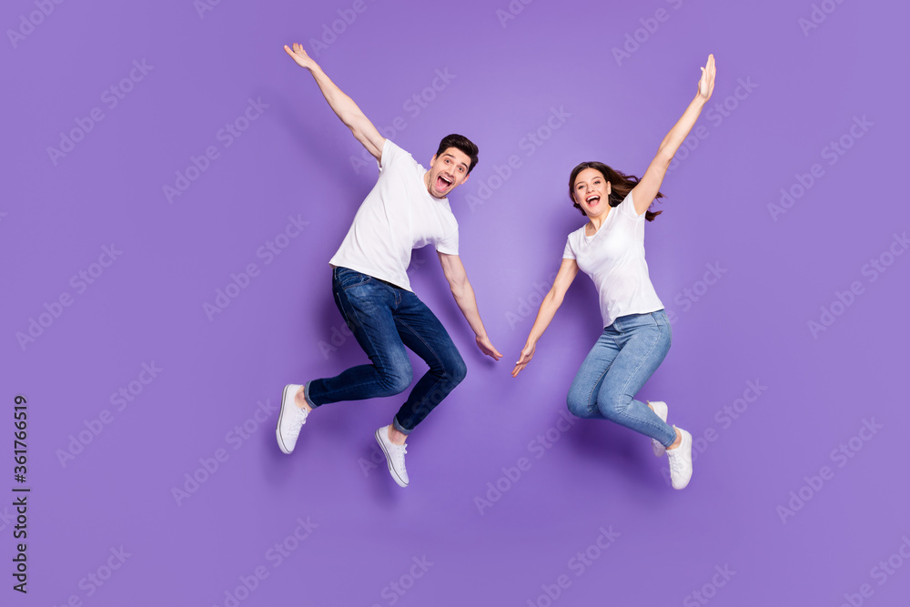 Full length photo of cheerful married couple man woman jump enjoy leisure free time rest wear casual style clothes sneakers isolated over violet color background