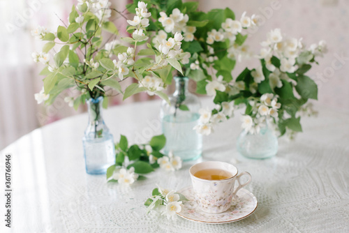 White blossom jasmine flowers in vase on the table with a cup of tea