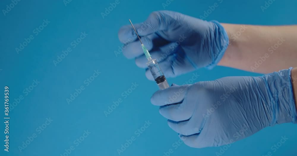 Close-up of a medic's hand in blue gloves with a medical syringe and a vaccine.