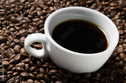 Cup of coffee drink sitting on a bed of roasted coffee beans background. Close up of a brown surface texture of aroma black caffeine drink ingredient for coffee beverage.