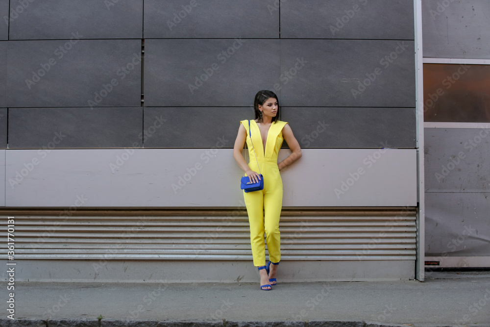 Outdoor portrait of young fashionable woman wearing a yellow jumpsuit and blue accessories Outdoor portrait of young fashionable woman wearing a yellow jumpsuit and blue accessories