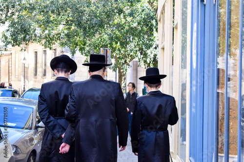 Fototapeta Naklejka Na Ścianę i Meble -  Three Hasidic Jewish men walk at a public street in Paris, France. Jewish or Judaic religious clothing. 