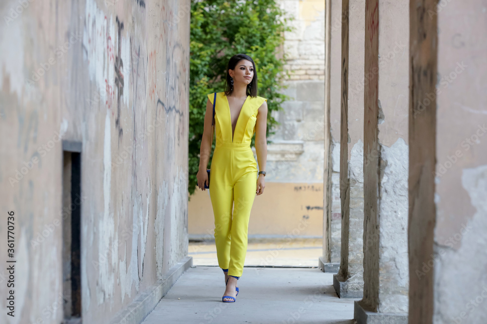 Outdoor portrait of young fashionable woman wearing a yellow jumpsuit
