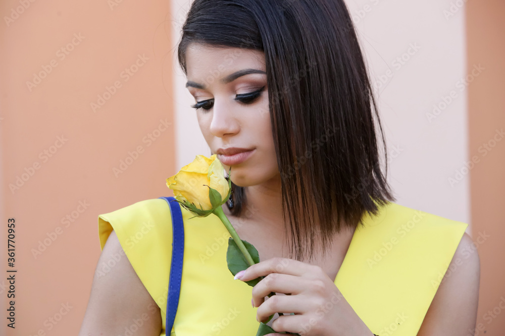 Close up portrait of young fashionable woman with dark long bob hairstyle in yellow outfit holding yellow rose flower. Close up portrait of young fashionable woman with dark long bob hairstyle in yellow outfit holding yellow rose flower.