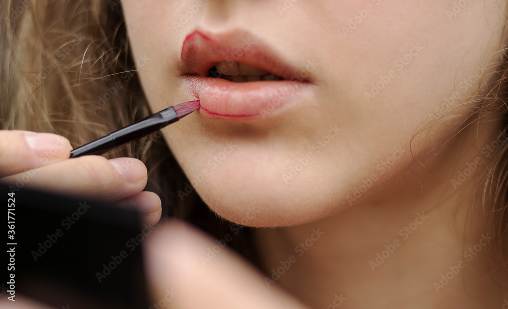 Beautiful woman is applying lipstick with a brush