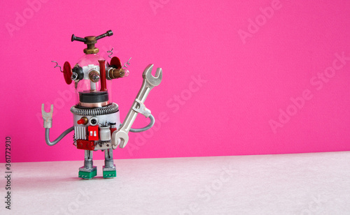 Toy robot mechanic holding a wrench tool in his hand. Pink background, copy space. Template for a poster with a repair service advertisement.