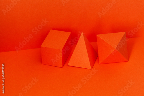Geometrical figures still life composition. Red pyramid rectangular cube objects on red background. Platonic solids figures, simplicity concept photography