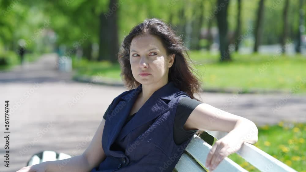 Portrait of beautiful brunette woman with long hair sitting on bench in public square on sunny spring day adult woman relaxes in park. Portrait of beautiful brunette woman with long hair sitting on bench in public square on sunny spring day adult woman relaxes in park.