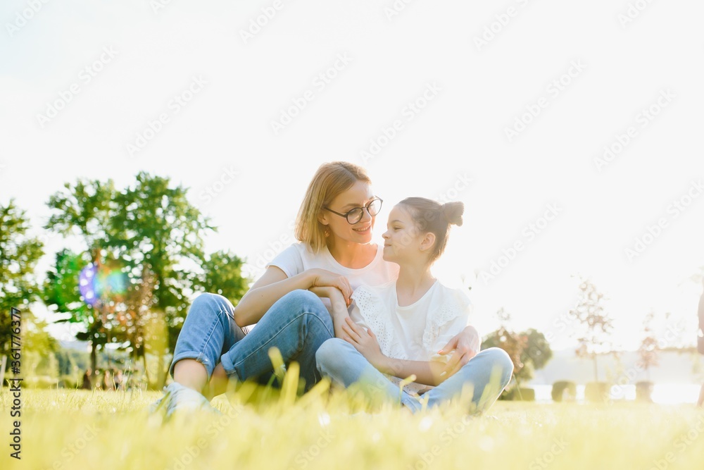 Fototapeta premium Happy and friendly family in nature. Emotional and young mother hugs her smiling little daughter lying on the grass. Summer park. Positive emotions.Childhood. Summertime.Lifestyle
