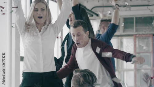 Young attractive team of business people dancing in the office on the table. Confetti falls on managers. Mans and womens dancing and having fun in the office. Slow Motion Video.