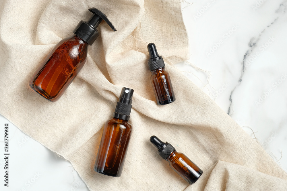Set of cosmetic amber glass bottles with beige fabric on marble table. Flat lay, top view. Beauty products for man skin care, natural organic cosmetics. Packaging mockup without labels. Set of cosmetic amber glass bottles with beige fabric on marble table. Flat lay, top view. Beauty products for man skin care, natural organic cosmetics. Packaging mockup without labels.