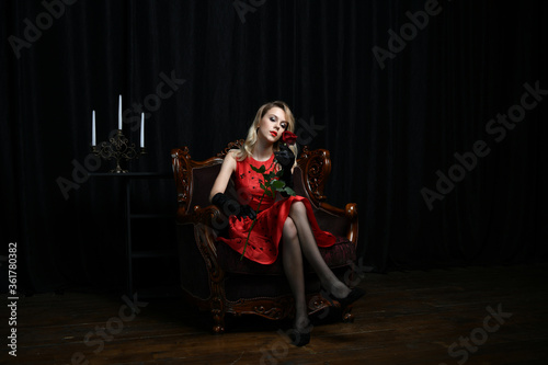 beautiful girl in a red dress posing in a chair with a red rose on a black background © константин константи