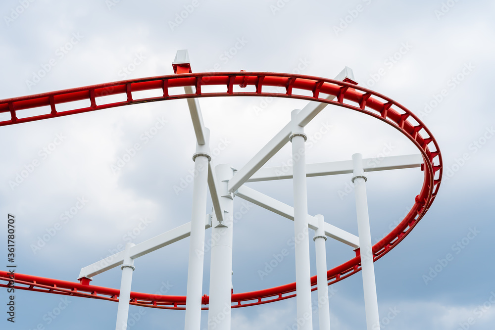 Red roller coaster in the amusement park, the background is a blue sky with white clouds