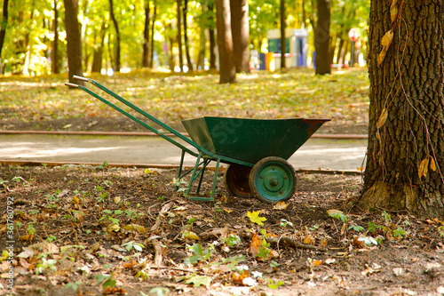 Side view of a green garden wheelbarrow during autumn work in the park. City park in the fall. Horizontal, cropped shot, free space. Concept of maintenance of city parks and gardens.
