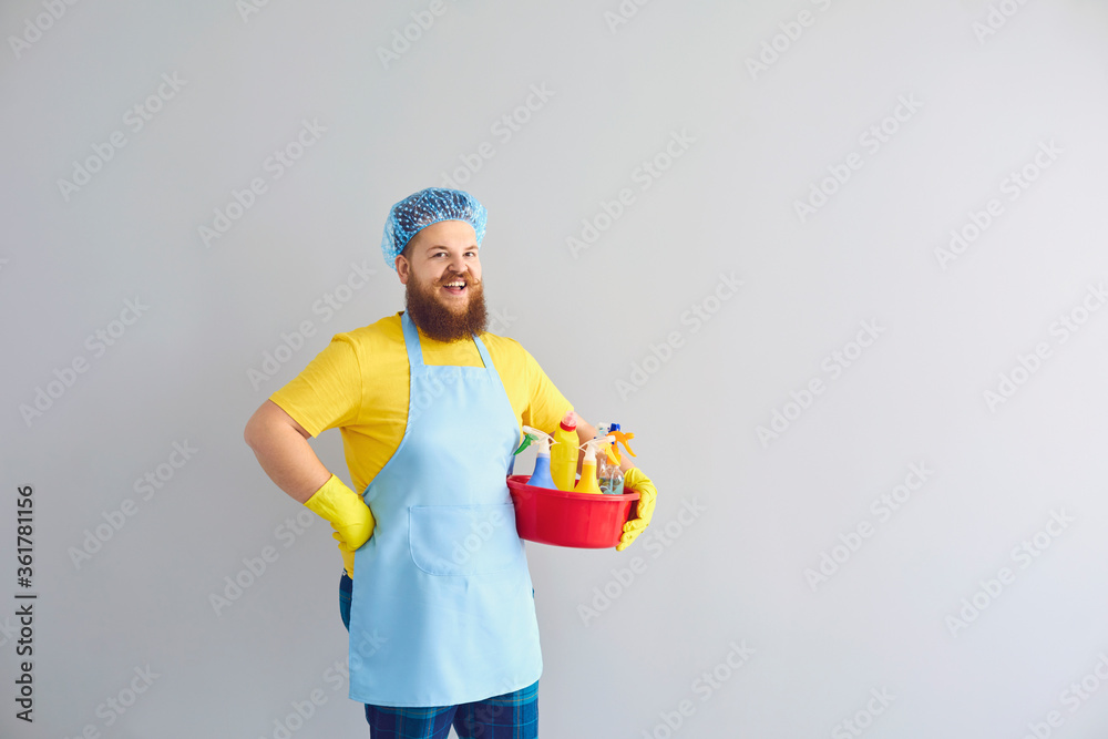 Funny fat guy with cleaning supplies on grey background, copy space. Sanitary service worker doing house chores Funny fat guy with cleaning supplies on grey background, copy space. Sanitary service worker doing house chores